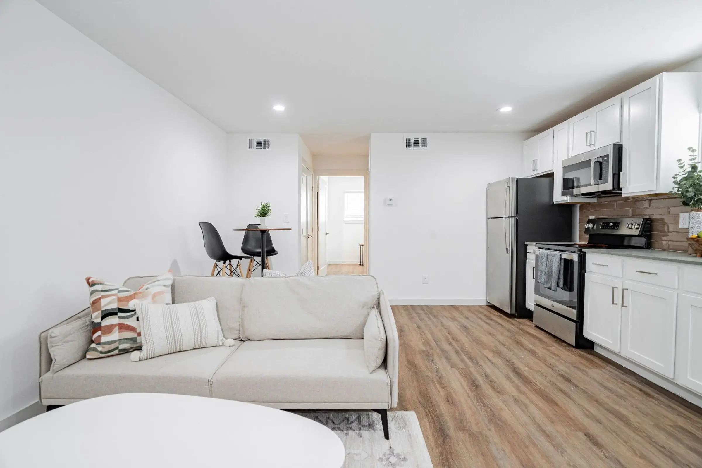 Modern Living Room and Kitchen Design A modern living room featuring a light-colored sofa with decorative pillows, a white coffee table, a dining area with two chairs, and an open kitchen with stainless steel appliances.