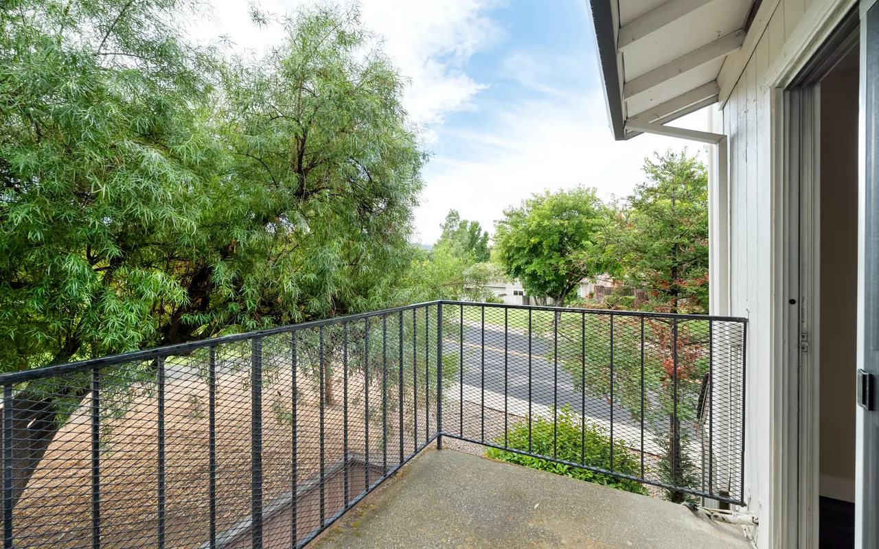 A view from a small balcony showing greenery and a road.