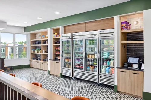 Modern Kitchen Area A modern kitchen area featuring open shelves filled with snacks, beverages in glass front refrigerators, and a stylish black and white patterned floor.