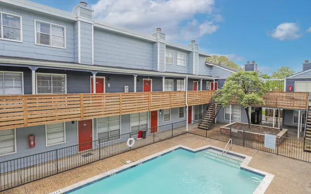 View of an apartment complex with a swimming pool in the foreground and balconies in the background.
