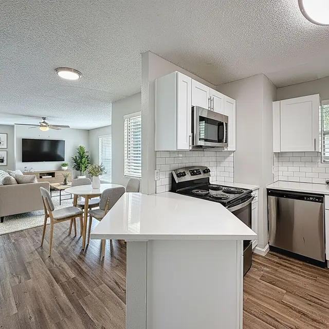 Modern Kitchen and Living Space A modern kitchen with white cabinets and stainless steel appliances, overlooking a cozy living area with a sofa and television.