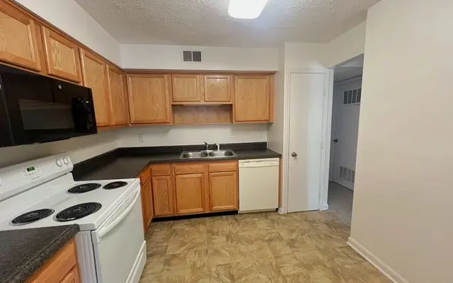 Modern Kitchen Interior A modern kitchen featuring wooden cabinets, black countertops, a sink with dishes, and appliances including a stove, microwave, and dishwasher.