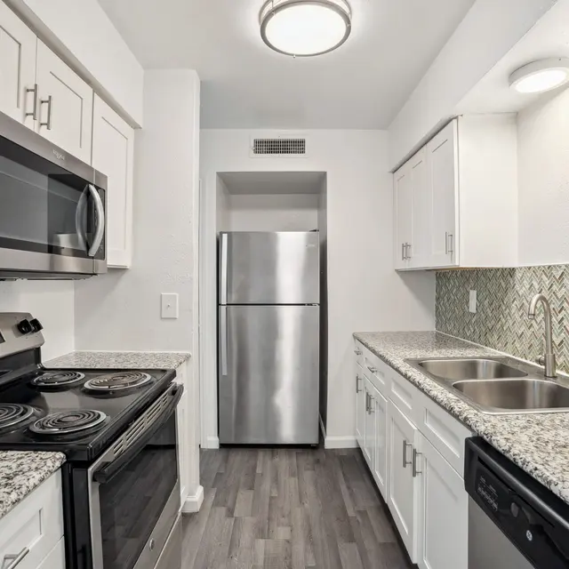 A modern kitchen featuring white cabinets, granite countertops, a stainless steel refrigerator, and a tiled backsplash with a chevron pattern.