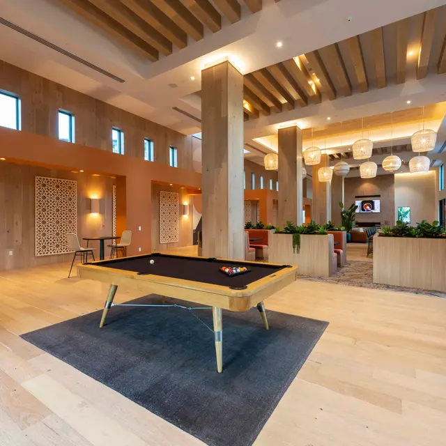 Modern Lounge with Pool Table A modern lounge area featuring a pool table in the center, surrounded by stylish furniture, wooden beams, and large windows providing natural light.