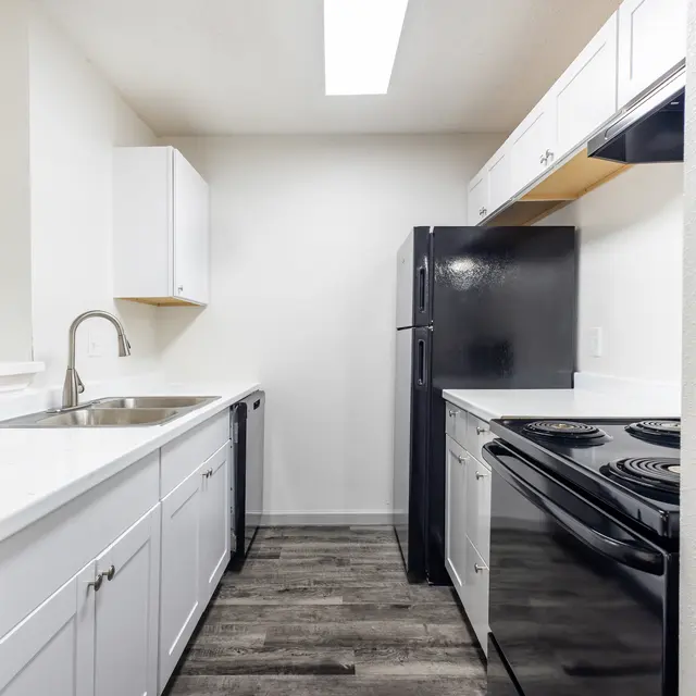A modern kitchen featuring a black refrigerator, stove, and a white sink with white cabinetry.