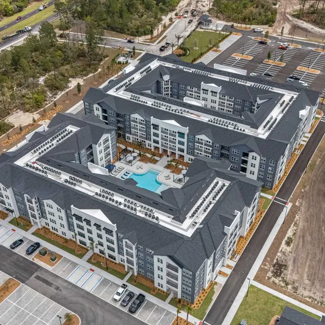 New Apartment Complex with Pool Aerial view of a newly constructed apartment complex with modern design and a swimming pool in the center. Surrounding areas include parking lots and green spaces.