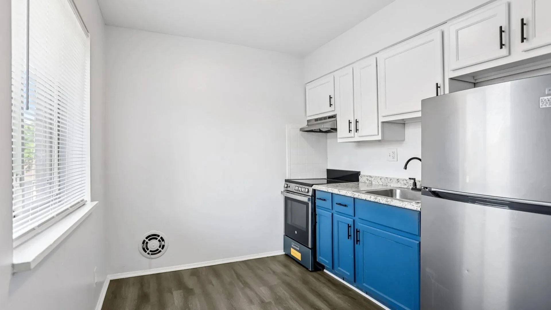 Modern Small Kitchen A small kitchen featuring white cabinets, a blue lower cabinet, an oven, a sink, and a stainless steel refrigerator, with a window allowing natural light.