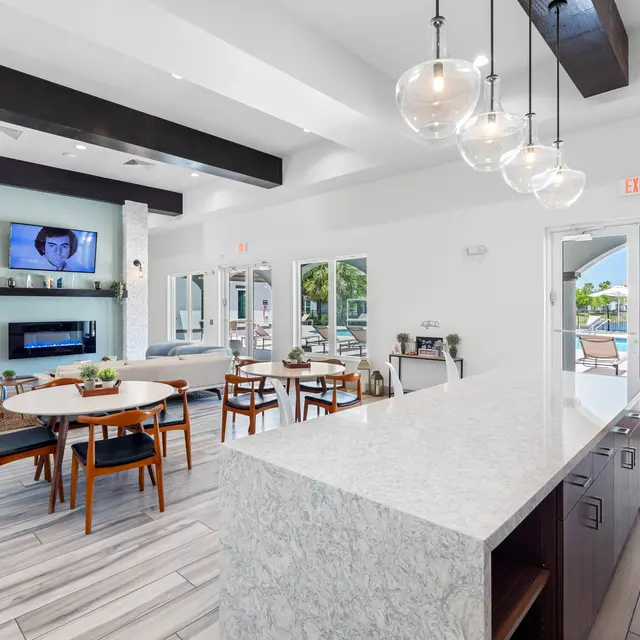 Stylish Lounge Area A modern lounge area featuring a white stone countertop, wooden tables and chairs, and large windows overlooking a pool.