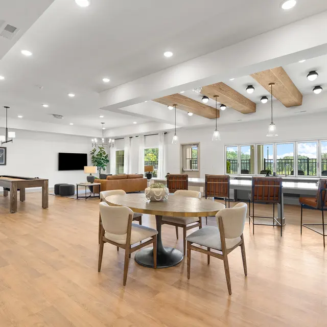 Spacious lounge area with a pool table, dining table, and seating arrangements, featuring wooden beams and large windows.