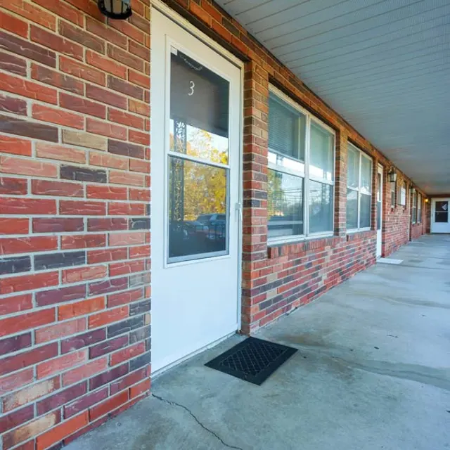 A view of a brick building's exterior, showing a row of doors along a sidewalk with a railing.