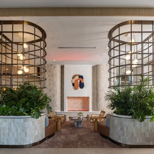 A modern lobby featuring decorative columns, greenery, and a fireplace.