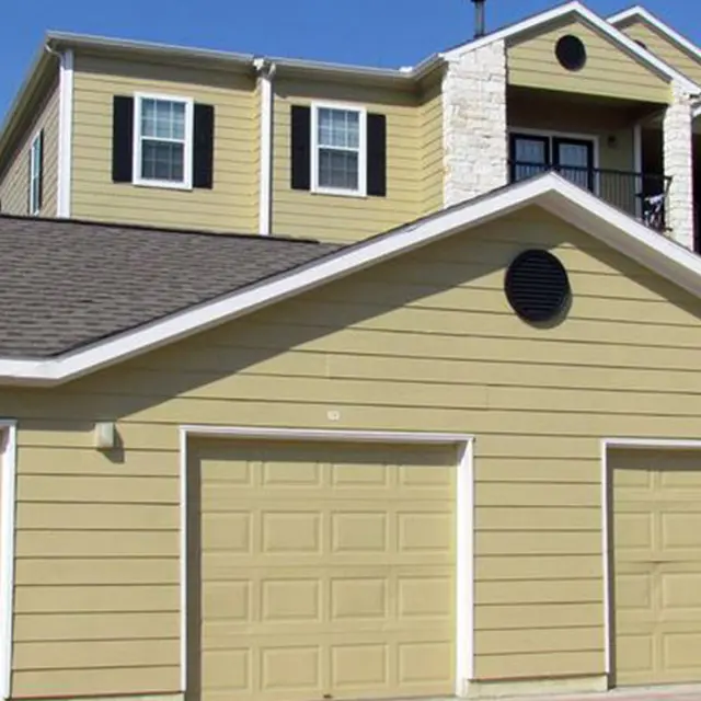 A row of three closed garages beneath a two-story yellow apartment building with balconies.