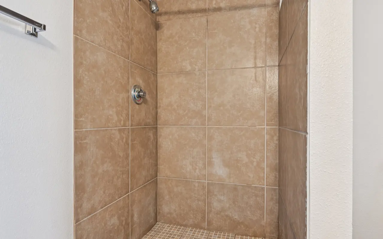 A tiled shower area with brown ceramic tiles on the walls, a showerhead, and a mosaic tile floor.