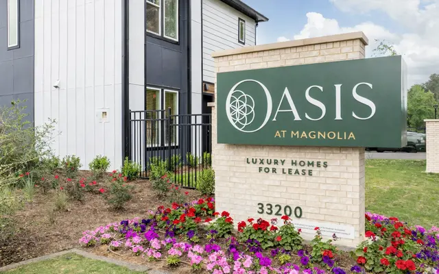 A decorative sign for 'Oasis at Magnolia' displaying 'Luxury Homes for Lease' with a floral border in a residential area.