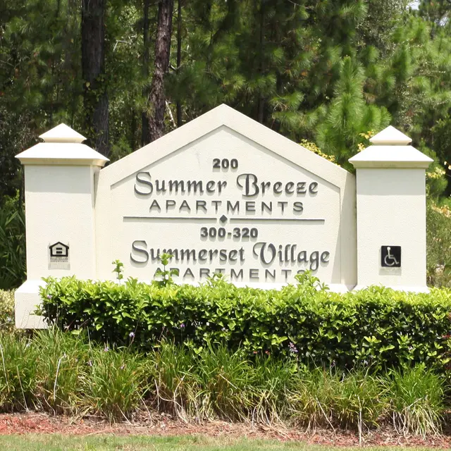 A sign displaying 'Summer Breeze Apartments' and 'Summerset Village Apartments' surrounded by greenery.