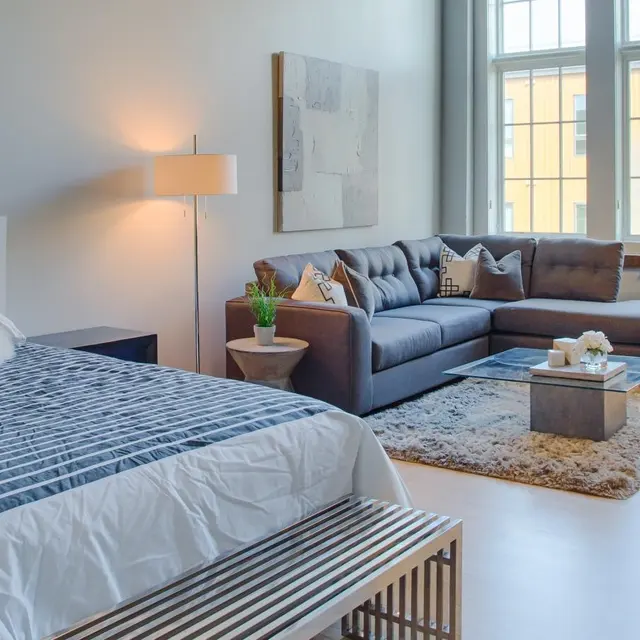 Studio apartment at Woodrow Apartments in Fargo featuring a queen bed, modern sectional sofa, large windows, and natural light.