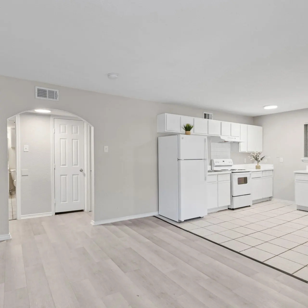 Bright and spacious interior of a modern apartment featuring a kitchenette with white appliances and light-colored flooring.