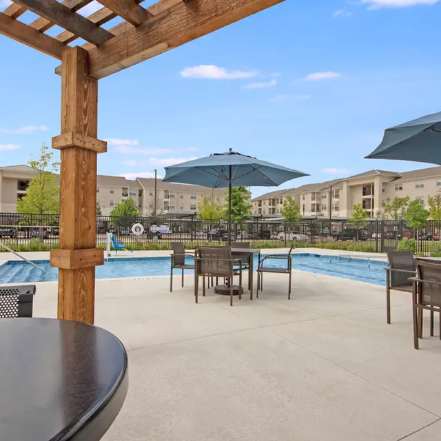 Apartment Complex Pool Area A swimming pool area at an apartment complex featuring patio tables, umbrellas, and a wooden pergola.