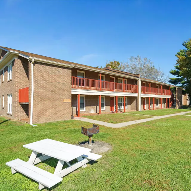 Exterior view of a two-story apartment complex surrounded by grass and trees.