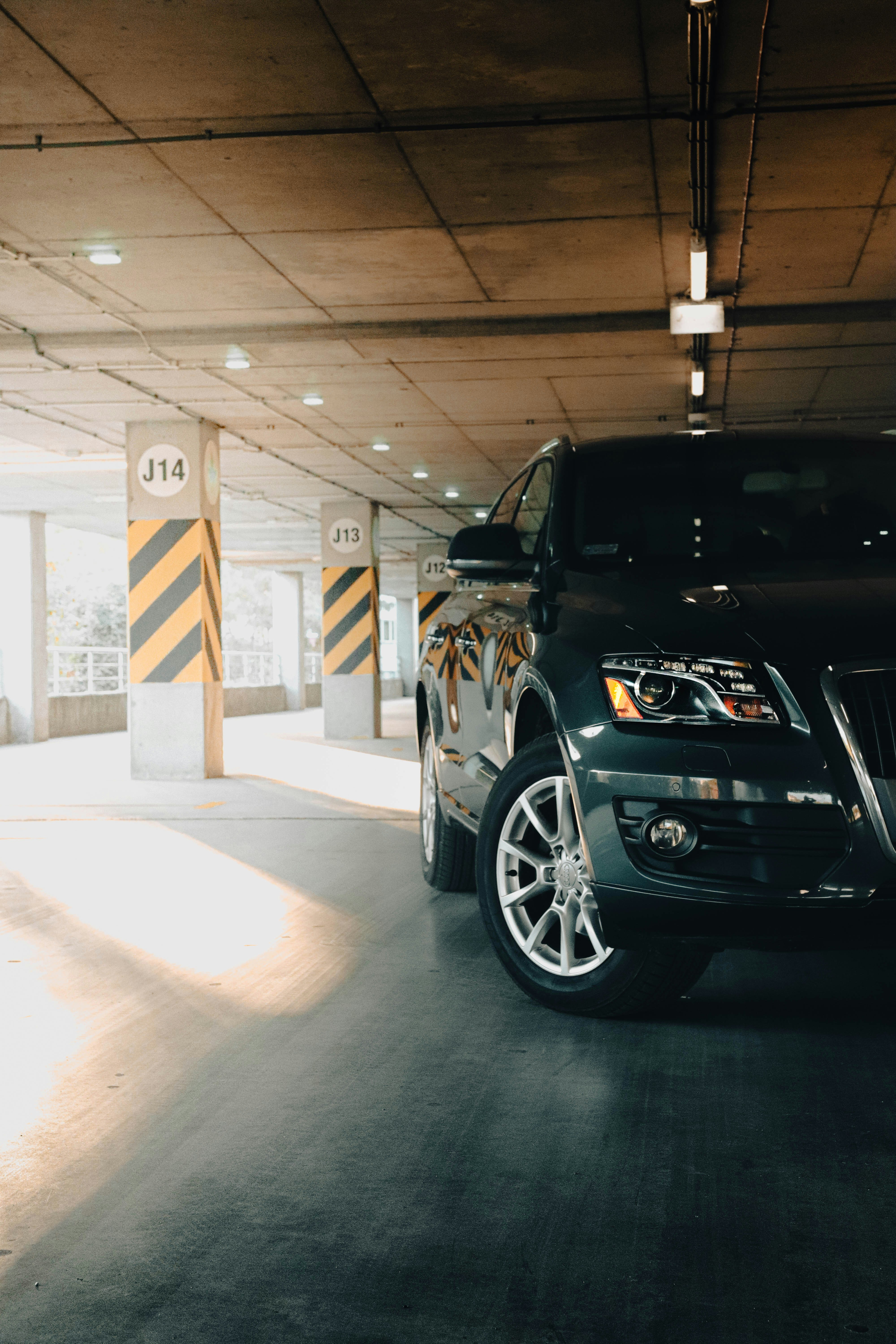 A dark-colored SUV parked in a modern parking garage, with yellow and black striped pillars and bright overhead lights.