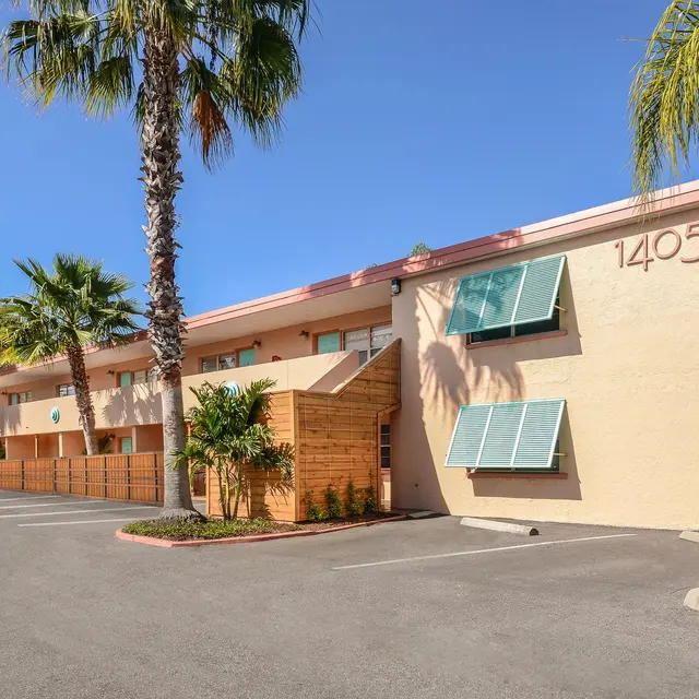 Exterior view of a three-story building with palm trees and blue sky.