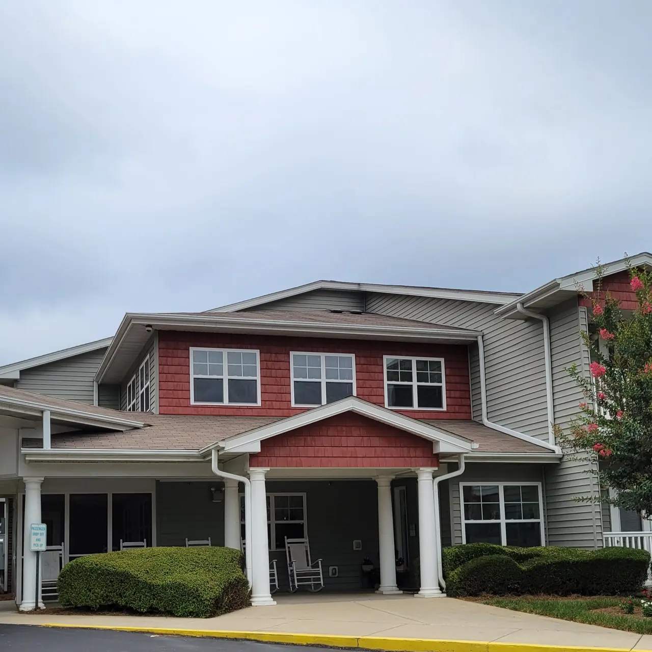 Exterior view of a senior living facility featuring a covered entrance and landscaped surroundings, with cloudy skies overhead.