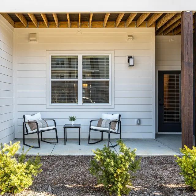 A cozy front patio with two chairs and a small table surrounded by plants and a clean concrete walkway.