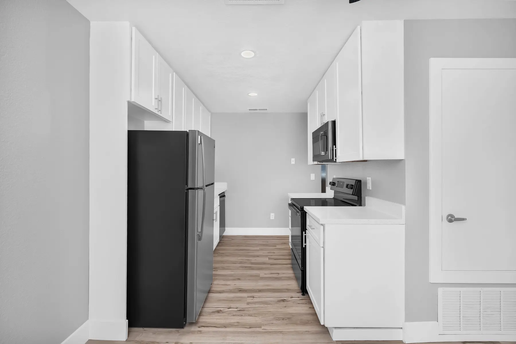 A modern kitchen featuring white cabinets, black appliances, and a light wooden floor.