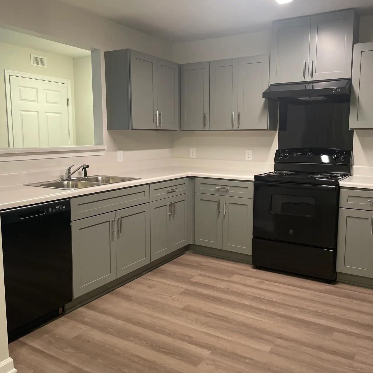 A modern kitchen featuring light gray cabinets, a black stove, and a black dishwasher, with wooden flooring.