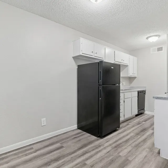 A modern kitchen with black appliances, including a refrigerator and dishwasher. White cabinets are above and light-colored flooring complements the space.