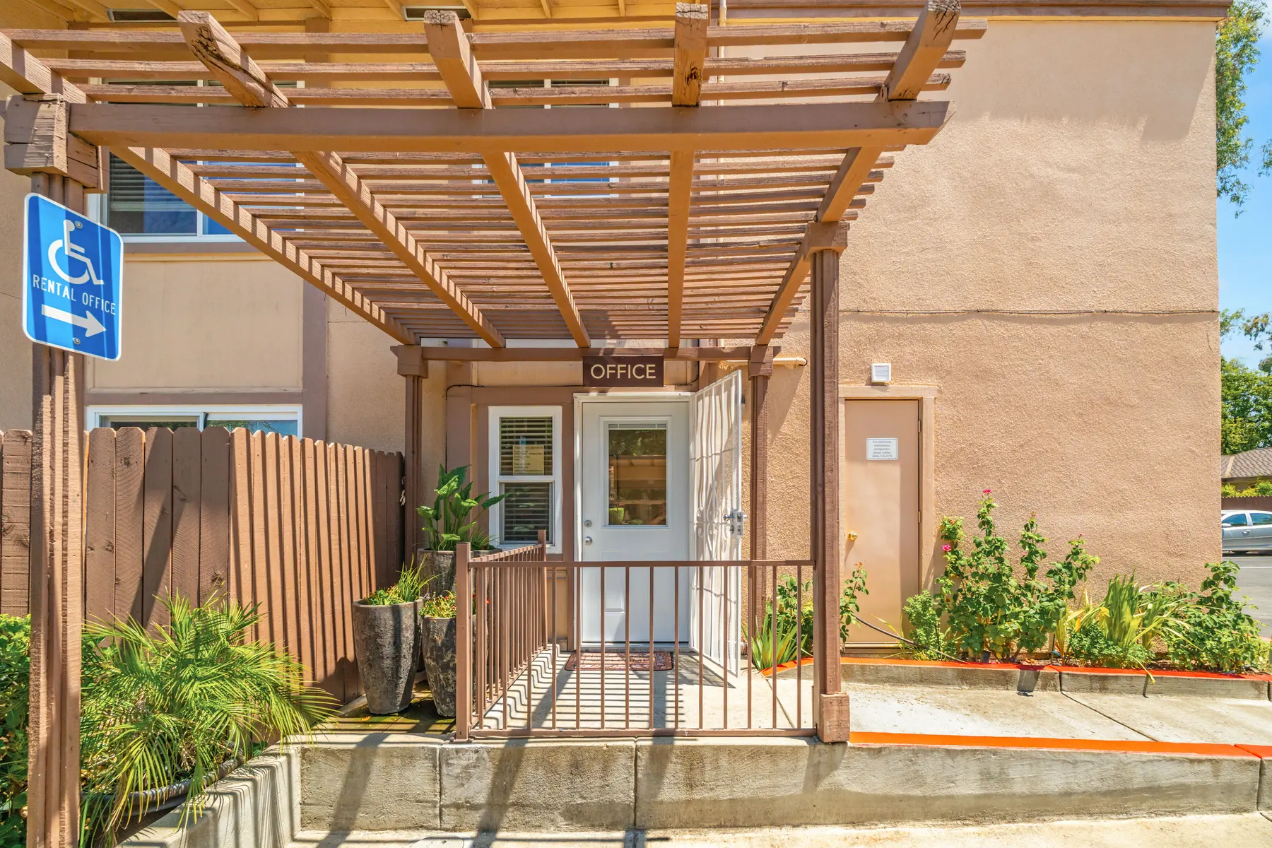 Exterior view of an office entrance with a wooden pergola, signage labeled 'OFFICE', and a handicap accessible sign.