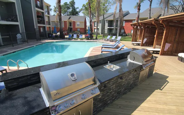 Spacious Apartment Complex Pool and Grill Area A view of a swimming pool surrounded by lounge chairs, with a grilling station in the foreground.