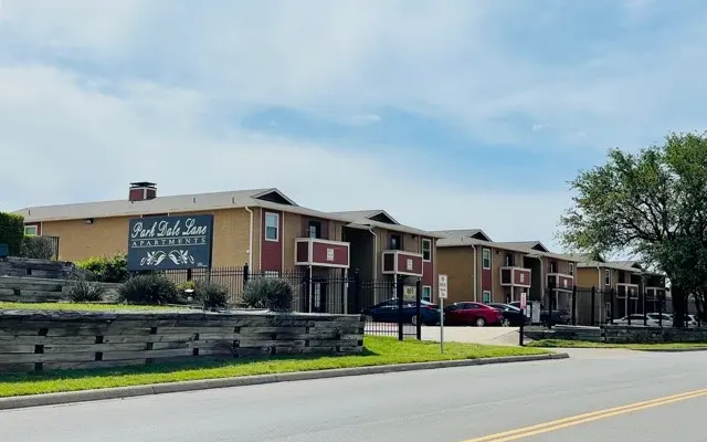 A view of a two-story apartment complex named Park Place Lane, featuring multiple units and a well-maintained exterior with greenery and a paved road in front.