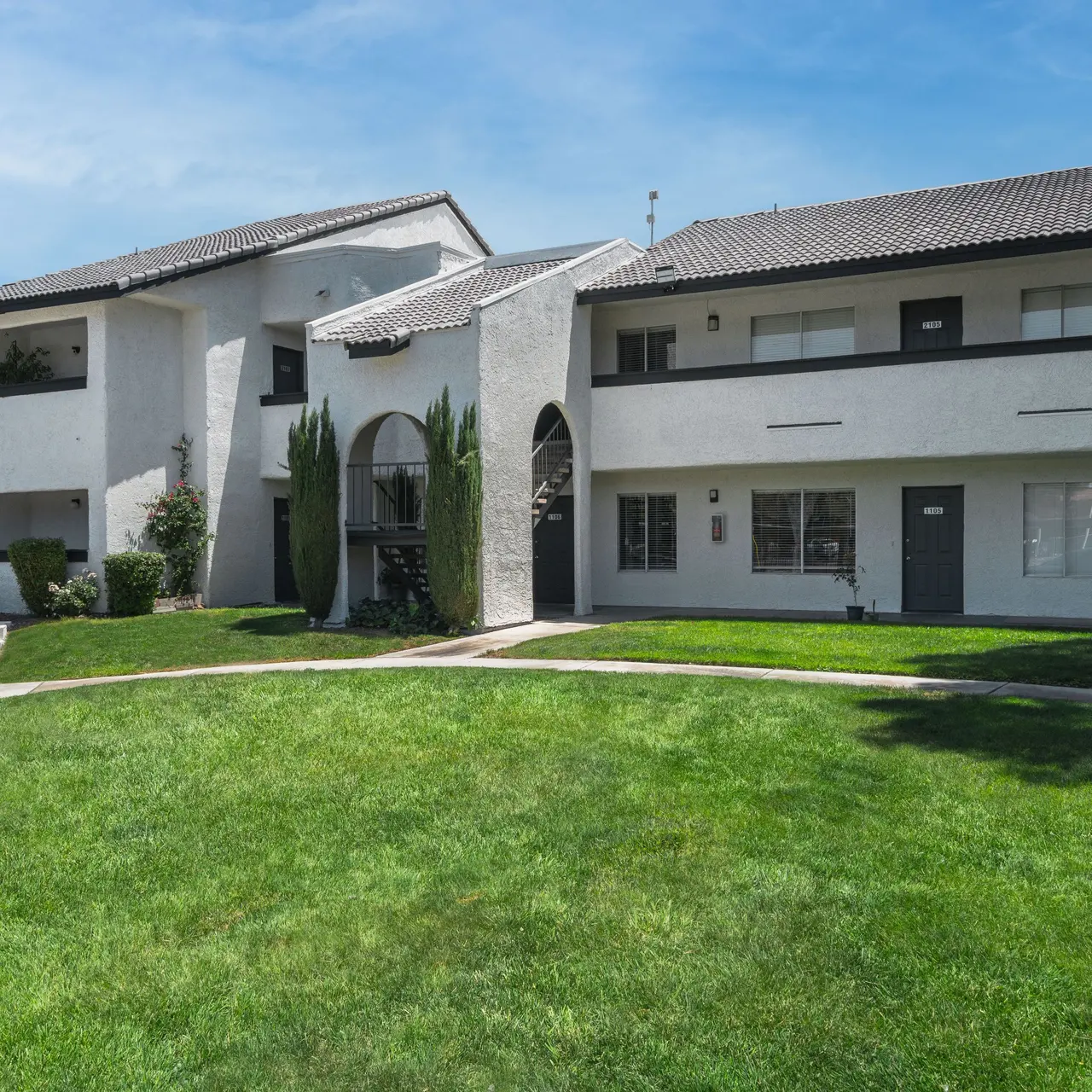 Exterior view of a two-story apartment complex with a landscaped lawn and clear blue sky.