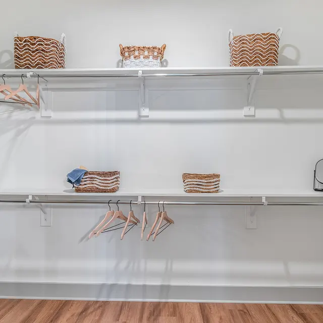 Organized Closet Space A spacious and organized closet featuring two shelves with decorative baskets and empty hangers on a rack against a white wall.
