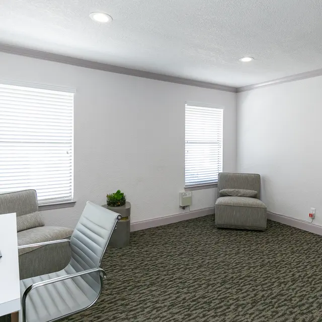 A simple and modern office space featuring a desk with a computer, an office chair, and two comfortable seating areas.