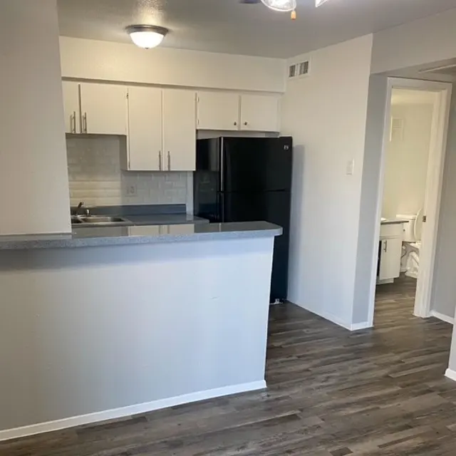 Interior view of a modern kitchen featuring white cabinets, a dark refrigerator, and laminate flooring.