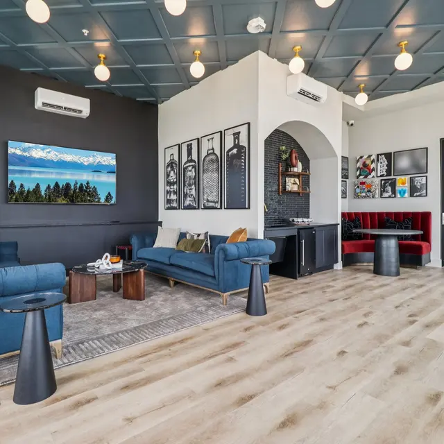 A modern living room with two blue sofas, wooden coffee table, and art on the walls. There is a large window with a view, and stylish lighting fixtures on the ceiling.