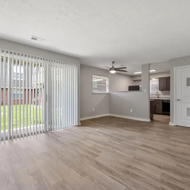 Spacious living area with wood-like floors, large windows, and a ceiling fan, opening to an outdoor view. Modern and bright.