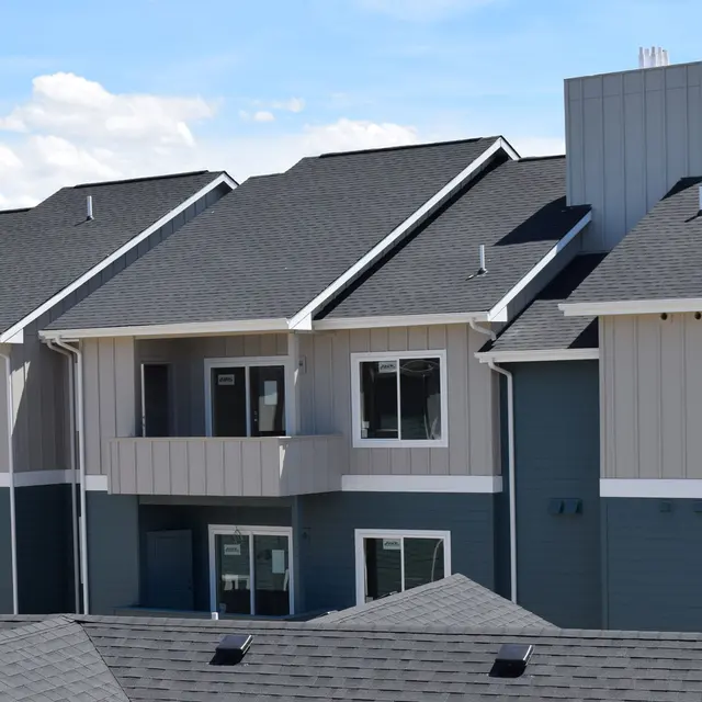 Canyon Terrace A modern apartment building featuring multiple units with varying colors of siding, new roofing, and large windows under a clear blue sky.
