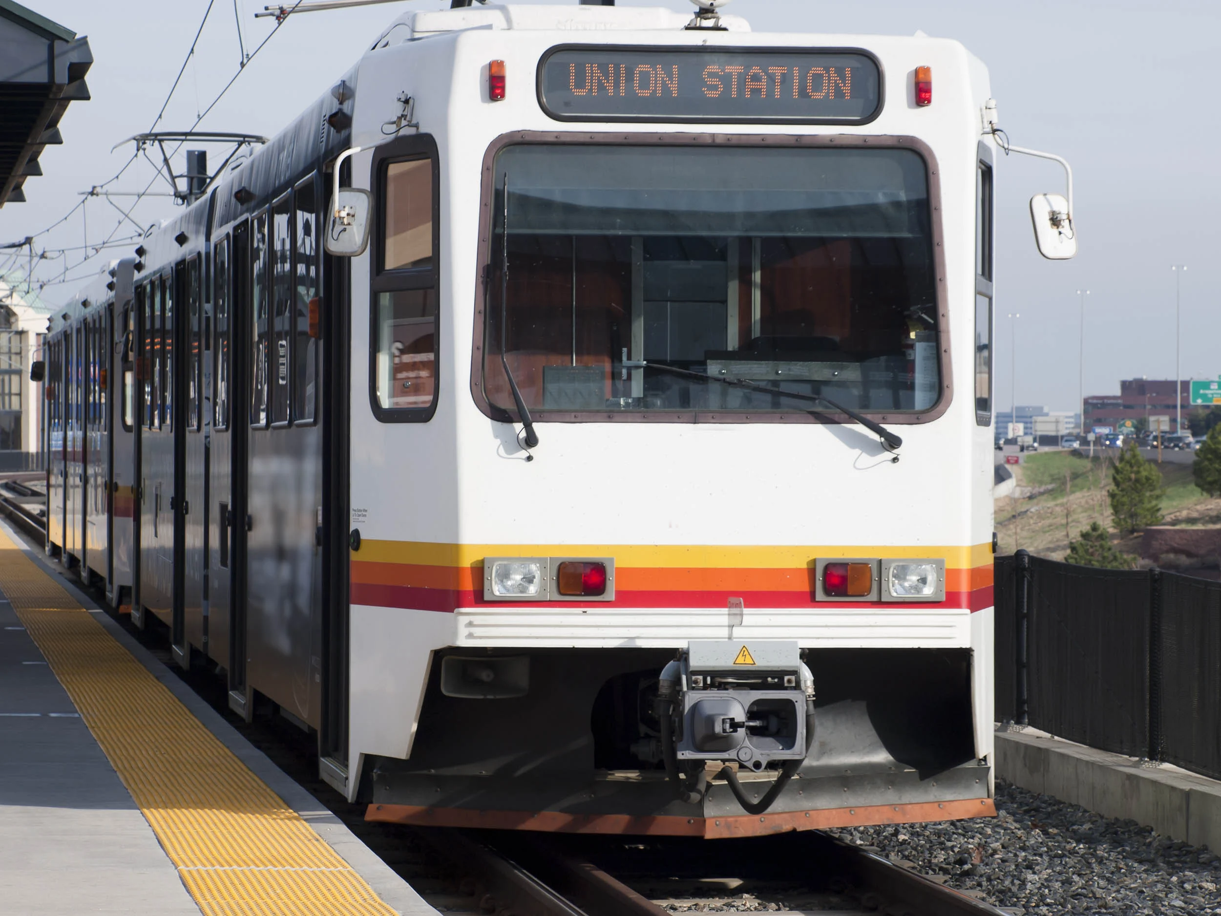 A light rail train at a station with the sign 'UNION STATION' displayed on the front. The train is white with a yellow stripe and is positioned on tracks with a platform visible.