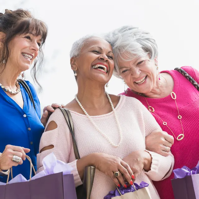 Three joyful women holding shopping bags and laughing together outdoors.