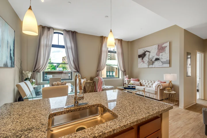 A modern apartment interior featuring a kitchen with granite countertops, a dining area, and a living room with a sofa and abstract art.