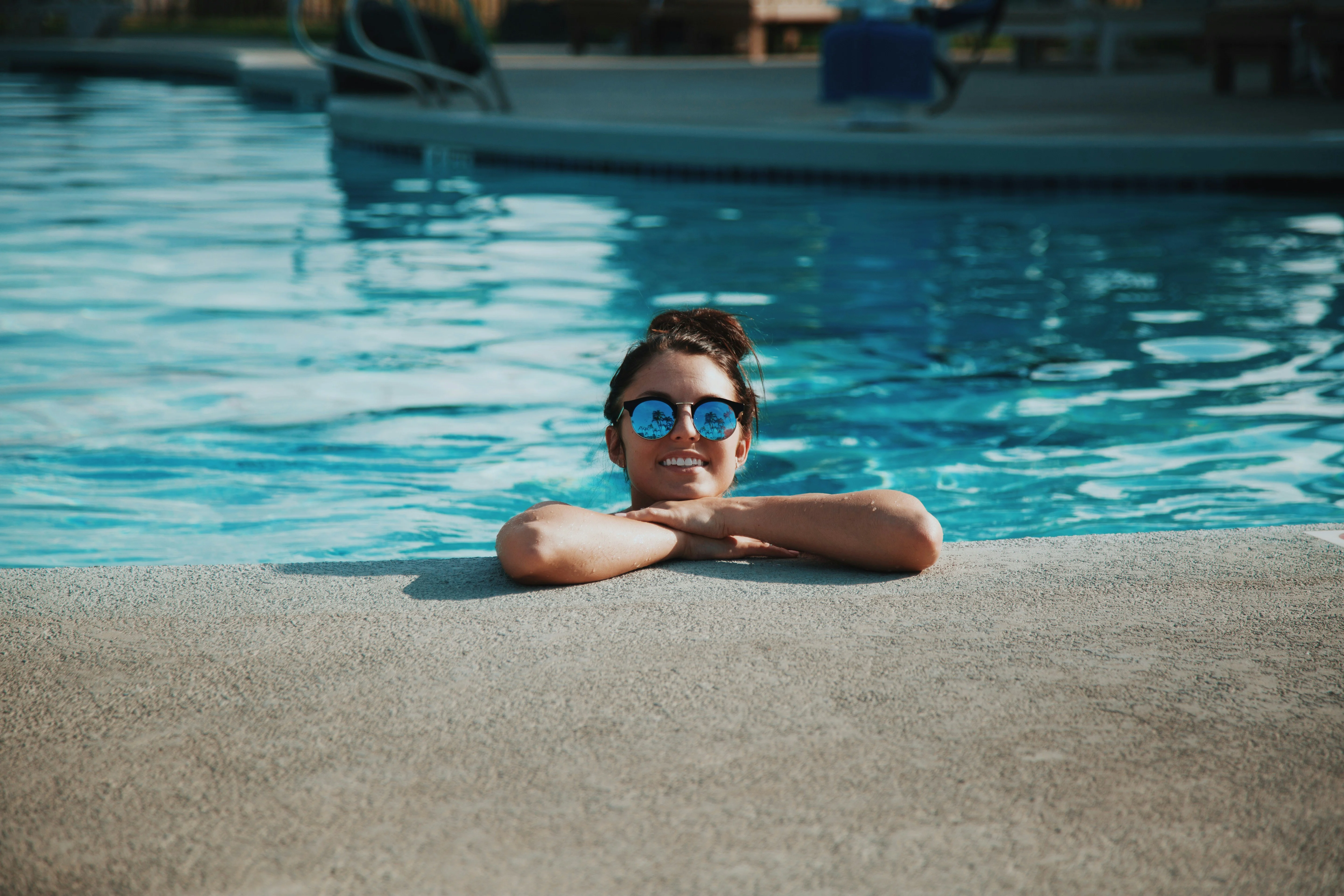 Refreshing Poolside Relaxation A person relaxing in a swimming pool, resting their arms on the edge while wearing sunglasses and smiling.