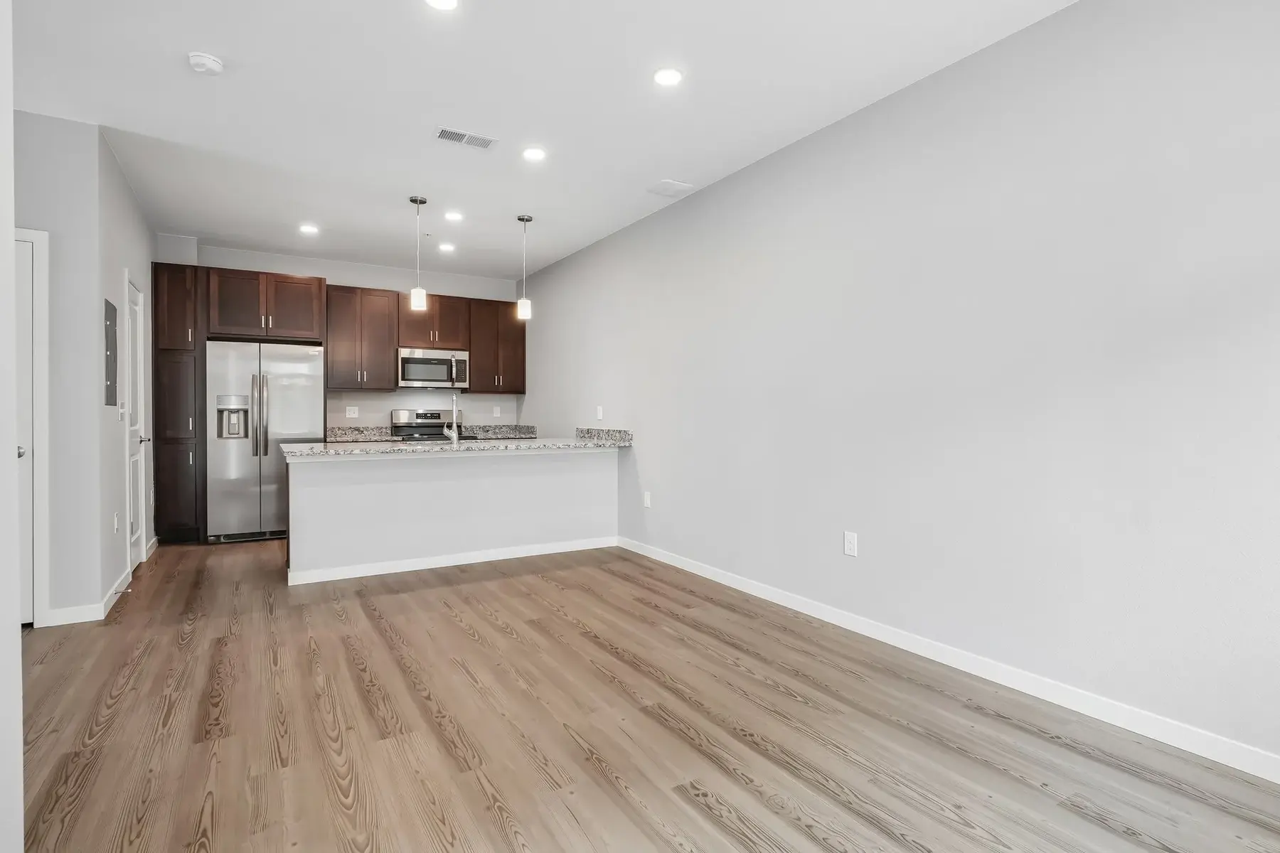 Modern Apartment Kitchen and Living Room A modern apartment interior featuring a kitchen area with brown cabinets, stainless steel appliances, and an open living space with wooden floors and neutral-colored walls.