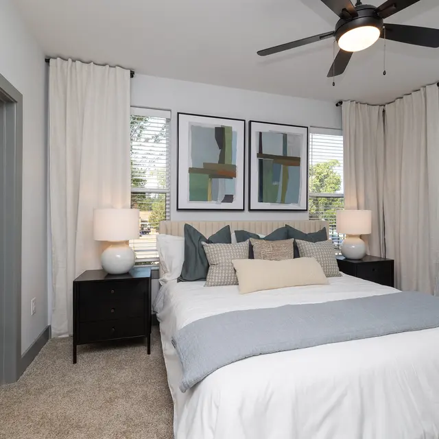 Modern Bedroom Interior A modern bedroom featuring a comfortable bed with decorative pillows, two nightstands with lamps, and large windows with white curtains overlooking greenery.