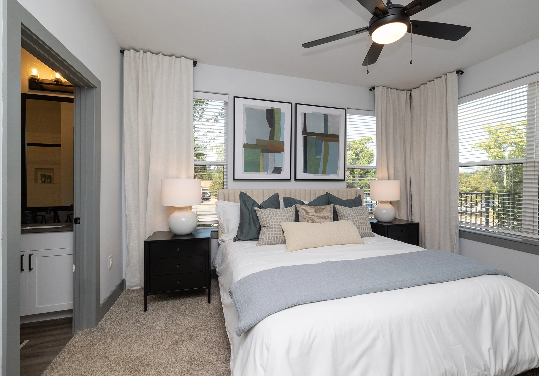 Modern Bedroom Interior A modern bedroom featuring a comfortable bed with decorative pillows, two nightstands with lamps, and large windows with white curtains overlooking greenery.