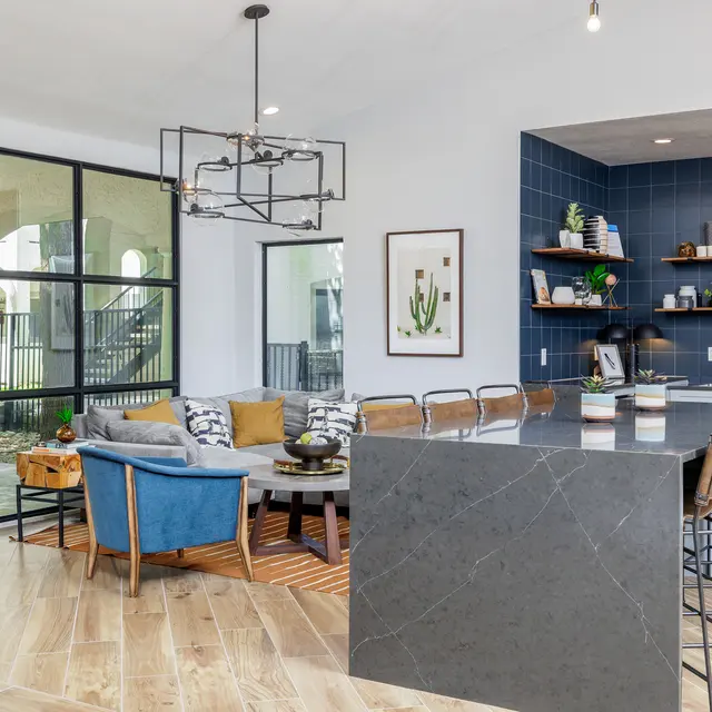 A modern living room and kitchen area featuring a large island with seating, a couch adorned with cushions, and large windows allowing natural light.