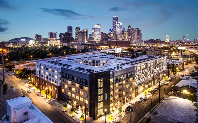 Aerial view of a modern apartment building at dusk with the Houston skyline in the background.