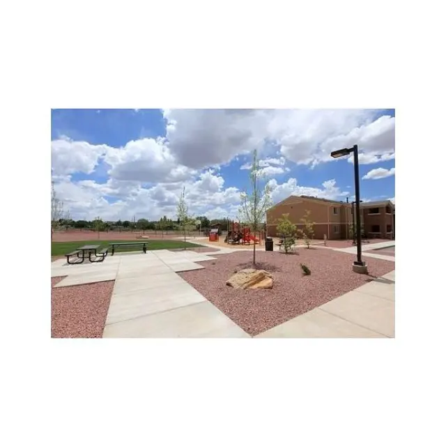 School Courtyard View View of a school courtyard featuring concrete pathways, landscaping with trees, and seating areas, under a bright sky with clouds.
